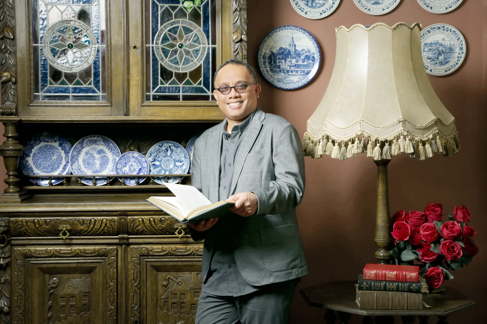 Anthon F. Susanto berdiri di dekat lemari antik sambil membuka sebuah buku